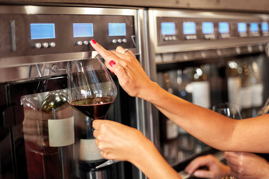 people, alcohol and lifestyle concept - close up of woman with glass pouring red wine from dispenser at bar or restaurant