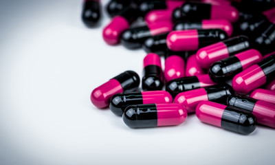 Pink-black capsule pills on white table. Antibiotics drug resistance. Global healthcare....