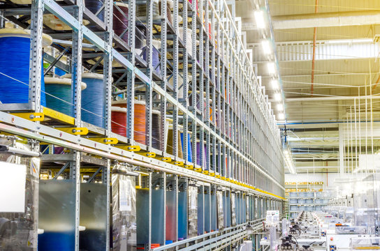 Large coils with colored electrical wires on huge shelves in an industrial plant. Manufacture of electrical wiring for cars. Employment in industry