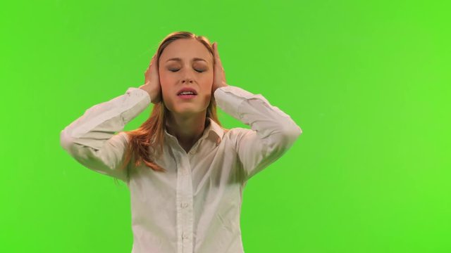 A disturb woman puts an earmuffs to protect her ears from noise, relaxes and smiles, over a green screen.