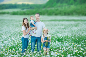 Fototapeta premium Young family in a field of flowers daises chamomile anjoy spa life happy together with cute faces in a village rustic motion
