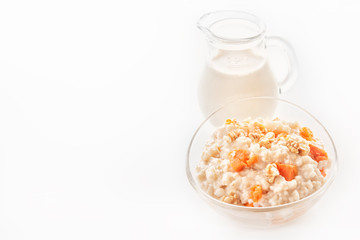 Oatmeal with pumpkin and nuts in a glass plate and a jug with milk on a white background. Close-up. Copy space