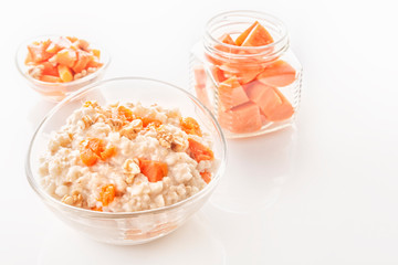 Fototapeta na wymiar Oatmeal with pumpkin and nuts in a glass plate and sliced carrots in a jar on a white background. Close-up. Copy space