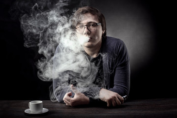 a man with glasses smokes an electronic cigarette and looks into the camera on a dark background