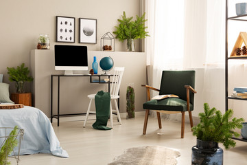 Urban jungle in bright bedroom interior with retro armchair and workspace with all in one computer and globe