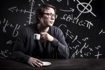 the teacher in glasses thoughtfully drinks coffee on the background of the blackboard with formulas