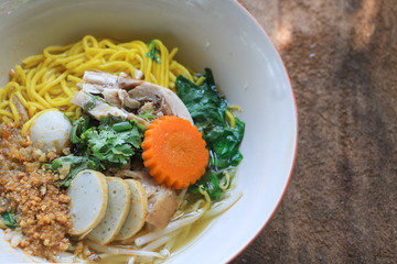 close up Thai yellow noodle soup with chicken and fishball, carrot and coriander in a bowl on wood table background.
