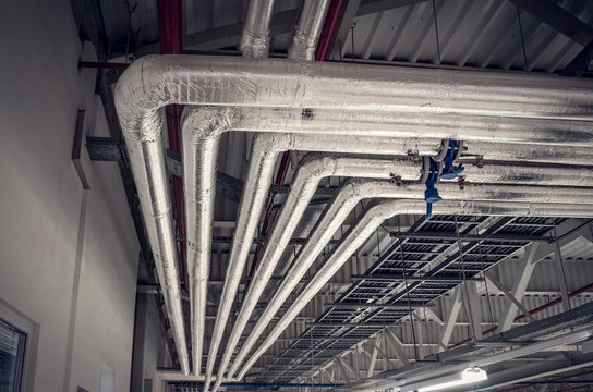 Metal Pipes In Thermal Insulation Winding On The Ceiling Of An Industrial Enterprise.