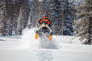 the guy is flying and jumping on a snowmobile on a background of winter forest  leaving a trail of splashes of white snow. bright snowmobile and suit without brands. extra high quality