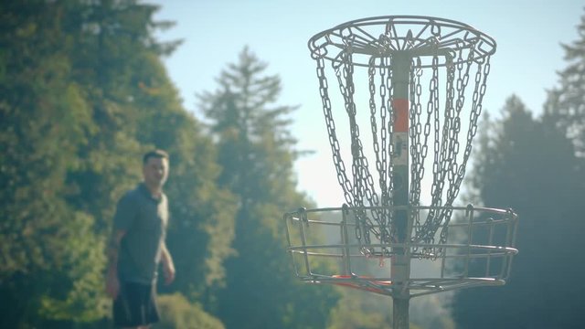 Man Throwing Disc into Basket at Frisbee Golf Course