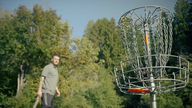 Man Practicing Frisbee Golf Throws Disc in Basket