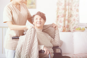 Senior care assistant helping elderly woman in the wheelchair at home