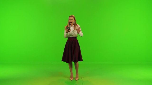 A stylish woman gets some amazing news on her phone, dances and kisses her phone happily over a green screen