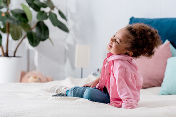 Fototapeta premium Curly African american kid sitting on the bed and smiling