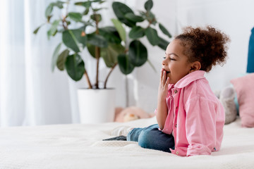 Cute yawning  African american kid sitting on the bed