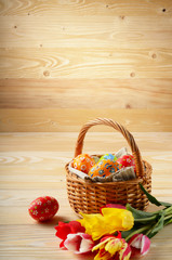 Fototapeta na wymiar Easter eggs in wicker basket and colorful tulip flowers on wooden table background with space for text