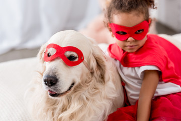 Adorable little african american kid with dog in superhero costumes and red masks