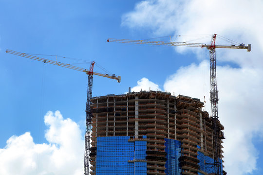 Construction industry image of tall cranes and building exterior in construction site over sunny sky in Florida, USA