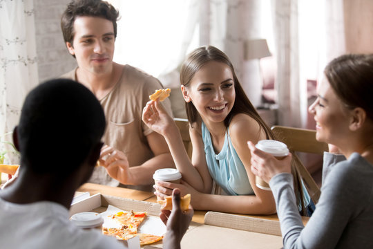 Diverse young cheerful millennial people having dinner sitting at table in pizzeria eating pizza feels happy. Best friends gathered together spending weekend together talking chatting communicating