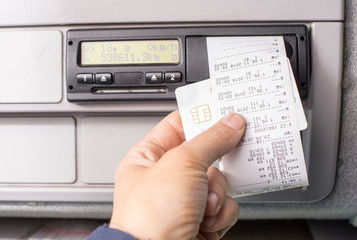 Digital tachograph and drivers hand holding print with driving times of the day
