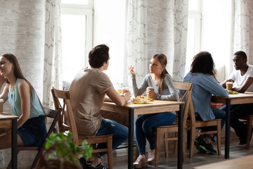 Inside of cozy cafeteria with wooden chairs tables in row, diverse multi-ethnic couples in love or best friends sitting drinking enjoying coffee during lunch in cafe chatting spending time on weekend