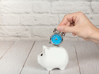 Saving time concept. Hand putting alarm clock into the piggy bank
