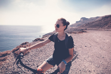 Young beautiful girl woman travels by bicycle on a mountain landscape on the beach in the sun,...