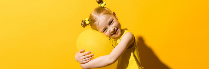 Girl with red hair on a yellow background. A girl is hugging a yellow balloon.