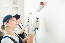 two beautiful women professionally paint the walls of the room. people in uniform, in overalls and a cap with a roller and brush, apartment renovation, interior design, tinting. isolated