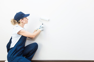 beautiful woman professionally paint the walls of the room. people in uniform, in overalls and a cap with a roller and brush, apartment renovation, interior design, tinting. isolated
