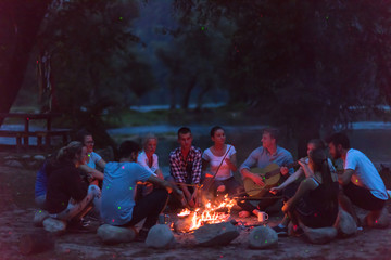 young friends relaxing around campfire - obrazy, fototapety, plakaty