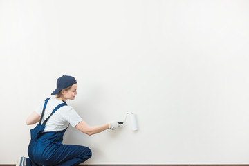 beautiful woman professionally paint the walls of the room. people in uniform, in overalls and a cap with a roller and brush, apartment renovation, interior design, tinting. isolated