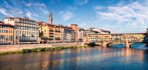 Fototapeta premium Sunny spring cityscape of Florence with Old Palace (Palazzo Vecchio or Palazzo della Signoria) on background and Ponte Vecchio bridge over Arno river. Colorful morning scene in Italy, Europe.