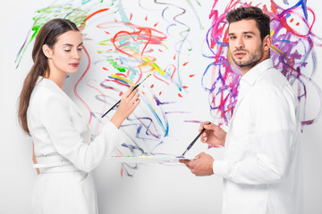 close up of adult couple in total white drawing with paintbrushes together on wall