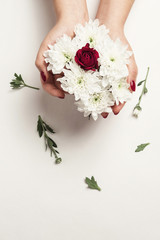 bouquet of chrysanthemums in the hands of a girl on a white background table, rose in center of bouquet