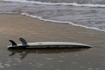 surfboard lying on the beach upside down near the shore line