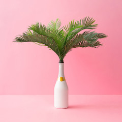 Champagne bottle with tropical green palm leaves on pastel pink background. Summer holiday concept...
