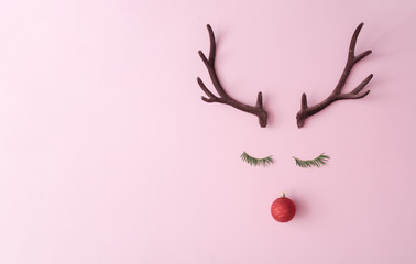 Fototapeta premium Christmas reindeer concept made of evergreen fir, red bauble decoration and antlers on pastel pink background. Minimal winter holidays idea. Flat lay top view composition.