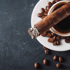 Cup of coffee, coffee beans, ashtray with cigar on dark background