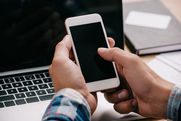 cropped shot of businessman using smartphone at workplace with laptop