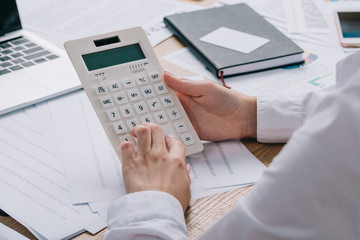 cropped shot of businesswoman making calculations on calculator at workplace with documents