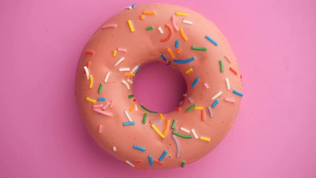 Bright and colorful sprinkled donut close-up shot spinning on a color background.
Top view. Seamless looping.
