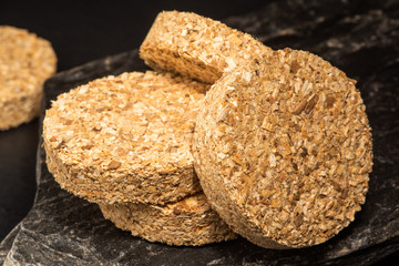 Stack of hardwood smoker bisquettes on black rock.