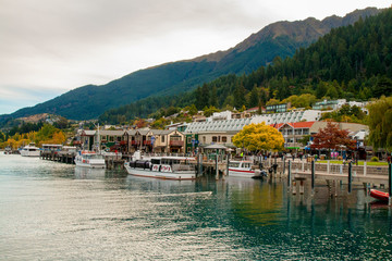 Fototapeta na wymiar Central part of Queenstown resort town on lake Wakatipu in Southern Alps, docked boats and lakeside city park, alpine architecture, colourful autumn in mountains, New Zealand