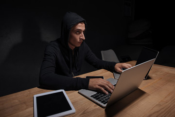 hacker in black hoodie using laptops in dark room, cyber security concept