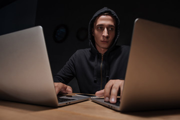 portrait of hacker in black hoodie using laptops in dark room, cyber security concept