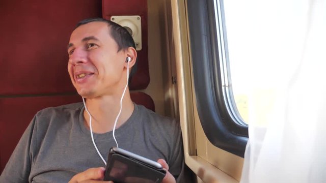 man listening to the music on lifestyle the train rail car coupe compartment travel. slow motion video. man with a smartphone at the window of a train in a car travel internet social media web. man