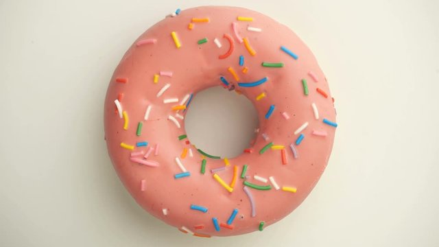 Bright and colorful sprinkled donut close-up shot spinning on a white background.
Top view. Seamless looping.
