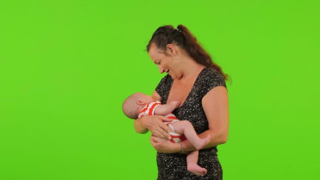 A young mom holds her newborn baby boy, trying to relax him over a green screen,