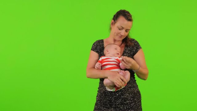 A beautiful young mom holds her newborn baby boy like Buddha and relaxes him over a green screen.